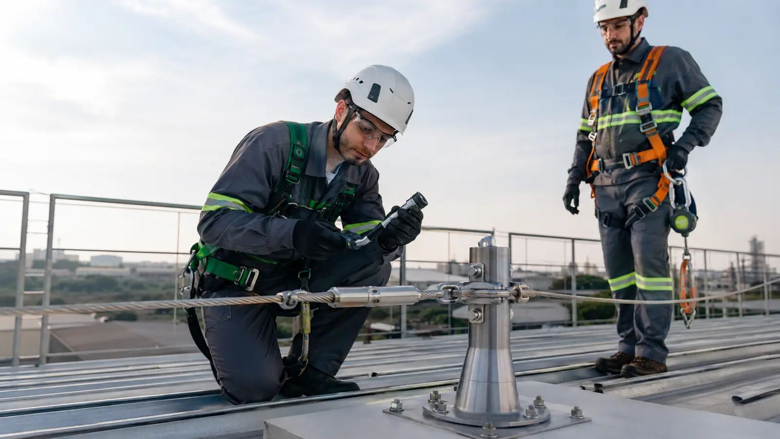 Engenheiros inspecionando ponto de ancoragem e cabo de linha de vida em cobertura industrial
